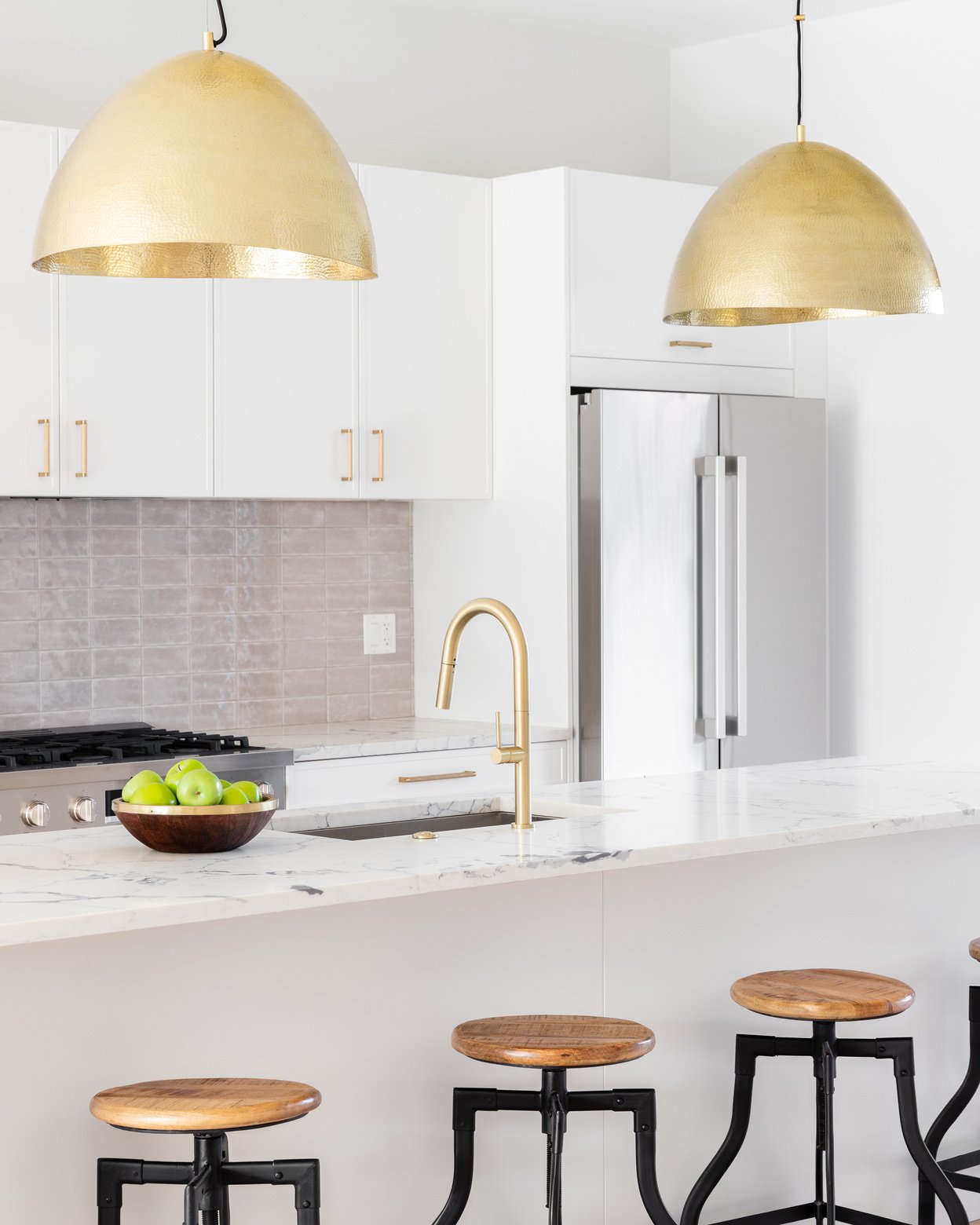 A kitchen detail of a white kitchen with gold lights and faucet.